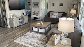 Una sala de estar moderna con una televisión de pantalla plana, un sofá gris, una mesa de centro y una lámpara.