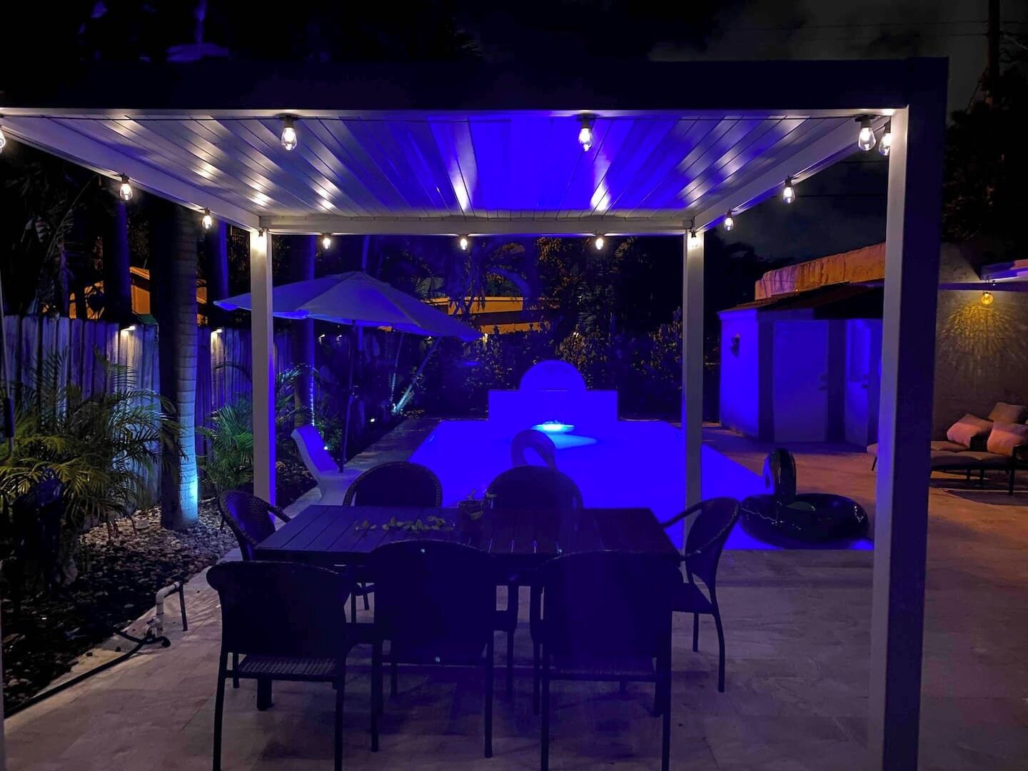 Backyard at night illuminated by beautiful solar lights and pool light.