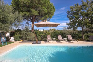 A swimming pool with clear water, surrounded by lounge chairs and a large umbrella. - TD Trulli Tortorella with Nature Pool & Sauna (Monopoli)