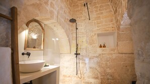 Une salle de bain avec un mur en pierre, un lavabo rond, un miroir et une douche.