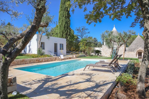 A swimming pool with lounge chairs, a white building, and stone structures in a landscaped garden. - TD Trulli Tortorella with Nature Pool & Sauna (Monopoli)