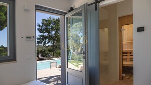 Une chambre avec une porte-fenêtre coulissante donnant sur une zone aménagée autour d’une piscine.