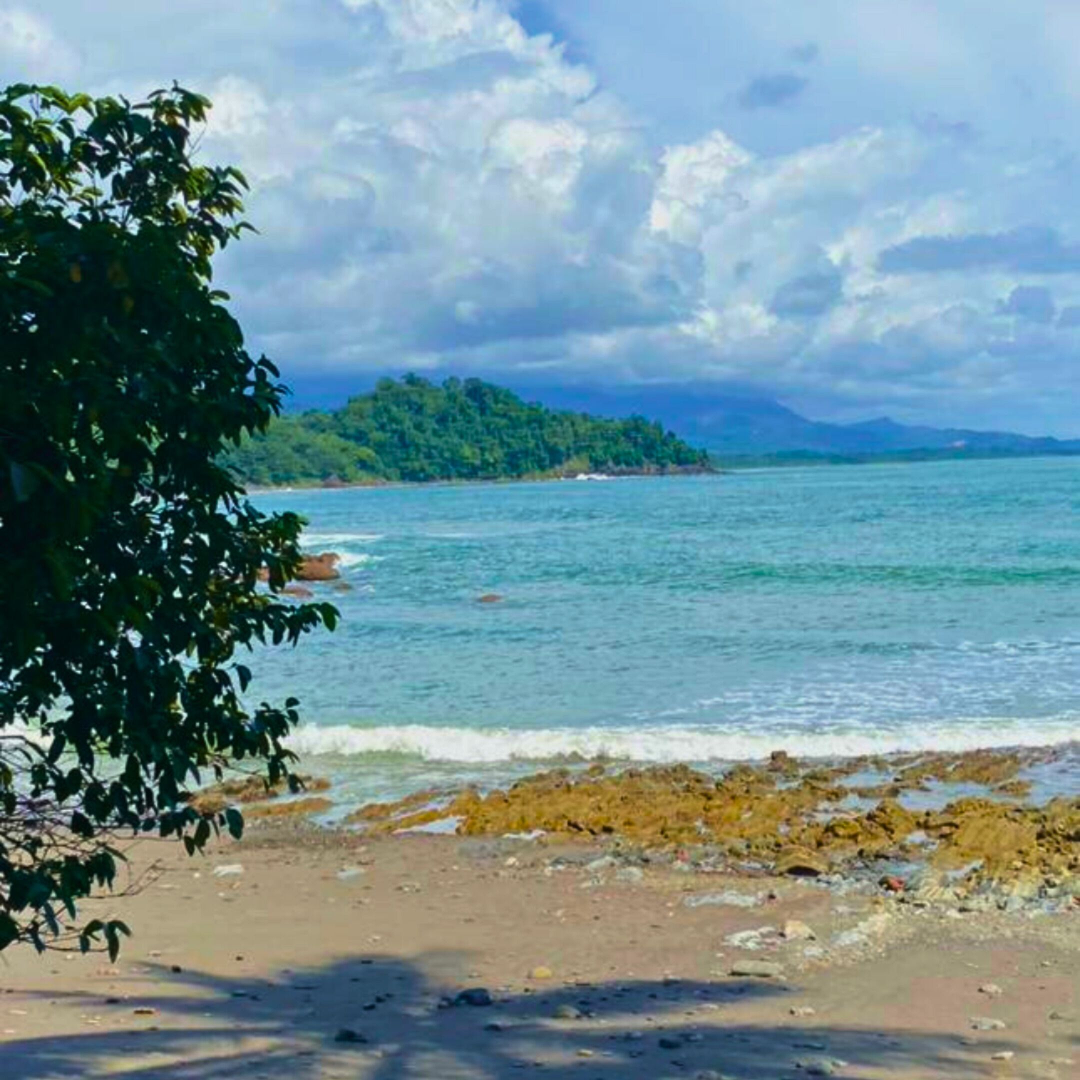 A beach with clear water, a distant island, and a cloudy sky.