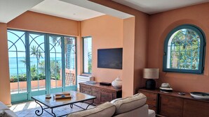 Amplia zona de estar con un gran ventanal que ofrece vistas al mar, un sofá acogedor, una mesa de centro y un mueble bajo con objetos decorativos.