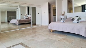 Un dormitorio con una cama grande, una mesita de noche, un espejo y un ventanal corredera que da a otra habitación.