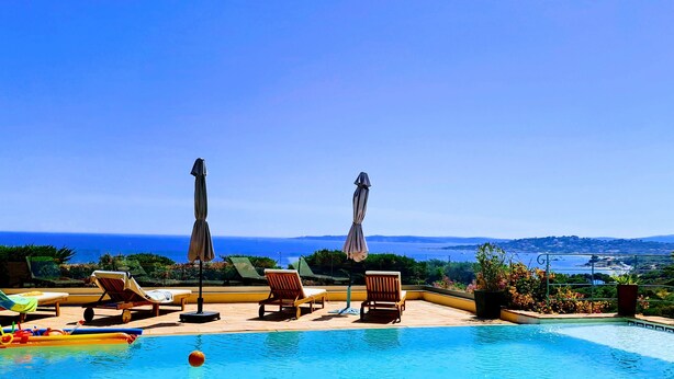 Zona de piscina con sillones de descanso y sombrillas, con vista panorámica al mar.