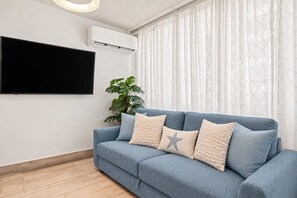 A living room with a blue sofa, a flat-screen TV mounted on the wall, and a potted plant.