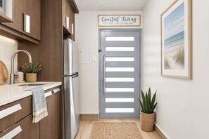 Une cuisine avec des meubles en bois, un réfrigérateur en acier inoxydable, un évier avec un torchon, et un panneau encadré au-dessus de la porte.