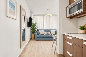 Un salon moderne avec un canapé bleu, un téléviseur à écran plat, une plante en pot et un coin repas avec une chaise blanche.