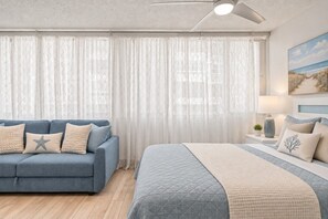 A bedroom with a bed, a blue sofa, and a nightstand with a lamp.