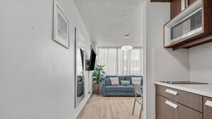 A modern kitchen with a microwave, wooden cabinets, and a dining area with a blue sofa and a plant. - Beachfront Cozy Loft  Walk 2 Eat Isla Verde Beach (Carolina)