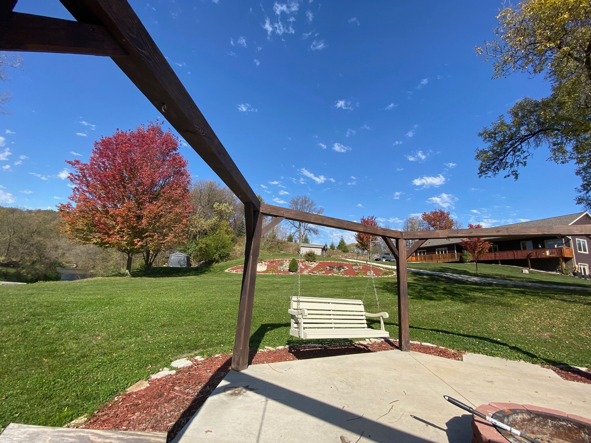 A patio area with a swing set, a concrete floor, and a wooden pergola.