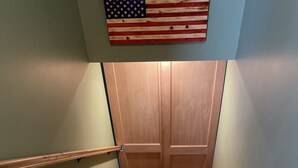 Un escalier en bois avec une rampe, une porte en bois en haut et un drapeau américain au-dessus.