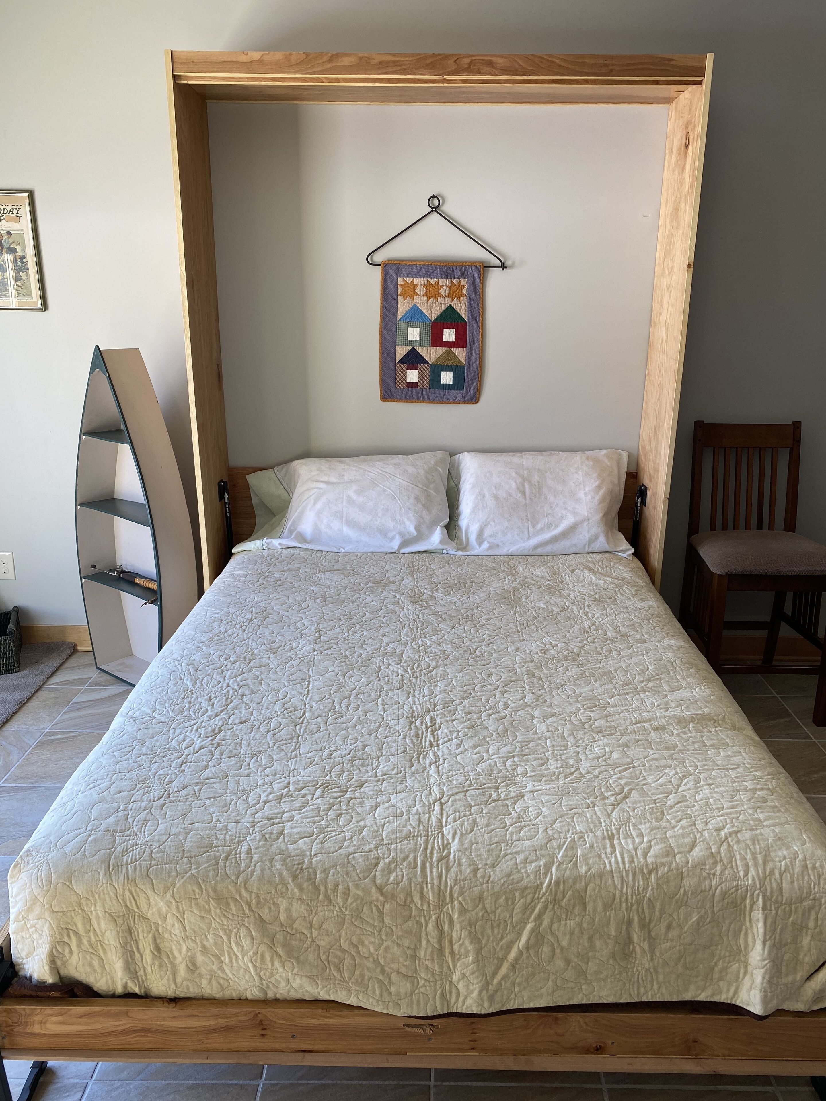 A bed with a quilted cover, a wooden headboard, and a quilted wall hanging above it.