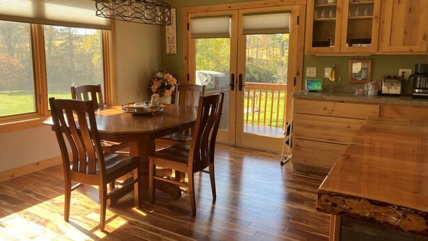 Un coin repas avec une table et des chaises en bois, un lustre et une vue sur une terrasse, accessible par une porte vitrée.