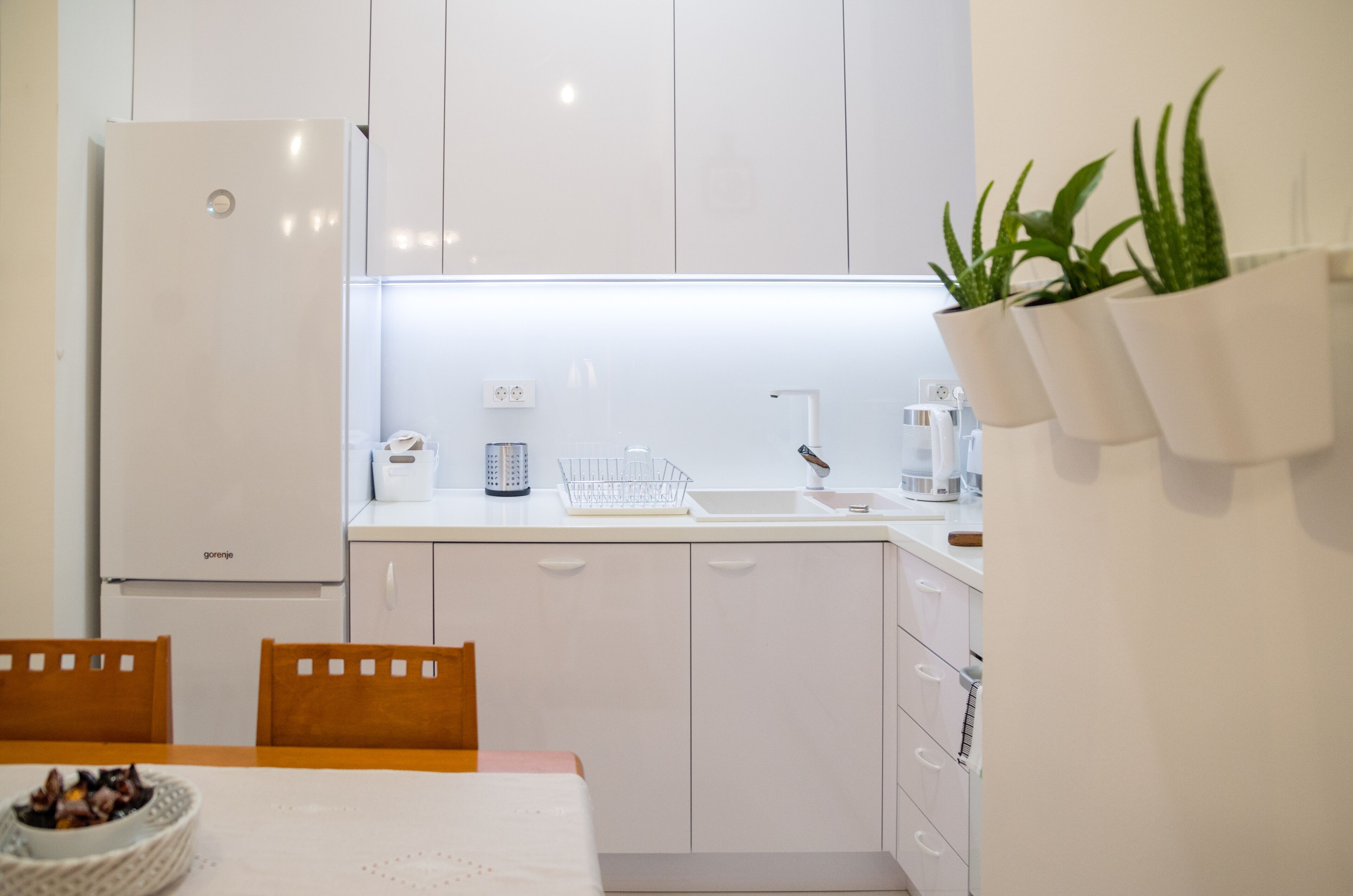 Une cuisine moderne avec des meubles blancs, un réfrigérateur, un évier et un coin repas comprenant une table et des chaises.