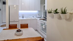 A modern kitchen with white cabinets, a dining table with chairs, and a refrigerator. - Sweet modern spot close to city center (Zagreb)