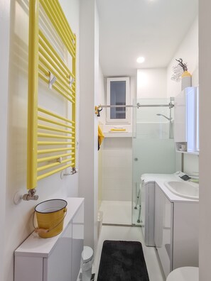 A modern bathroom with a yellow towel rack, a glass shower enclosure, and a white sink.