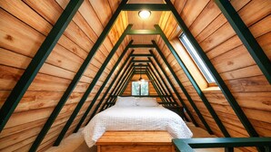 Un dormitorio acogedor en el ático con techo inclinado de madera, una cama central y un pequeño ventanal.