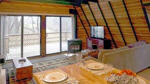 Una habitación acogedora y bien iluminada con una mesa de comedor para cuatro personas, un sofá y un televisor al fondo.