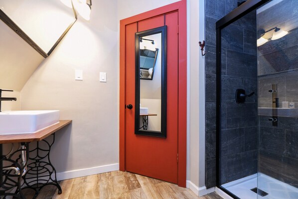 A bathroom with a red door, a white sink, a mirror, and a glass shower enclosure.