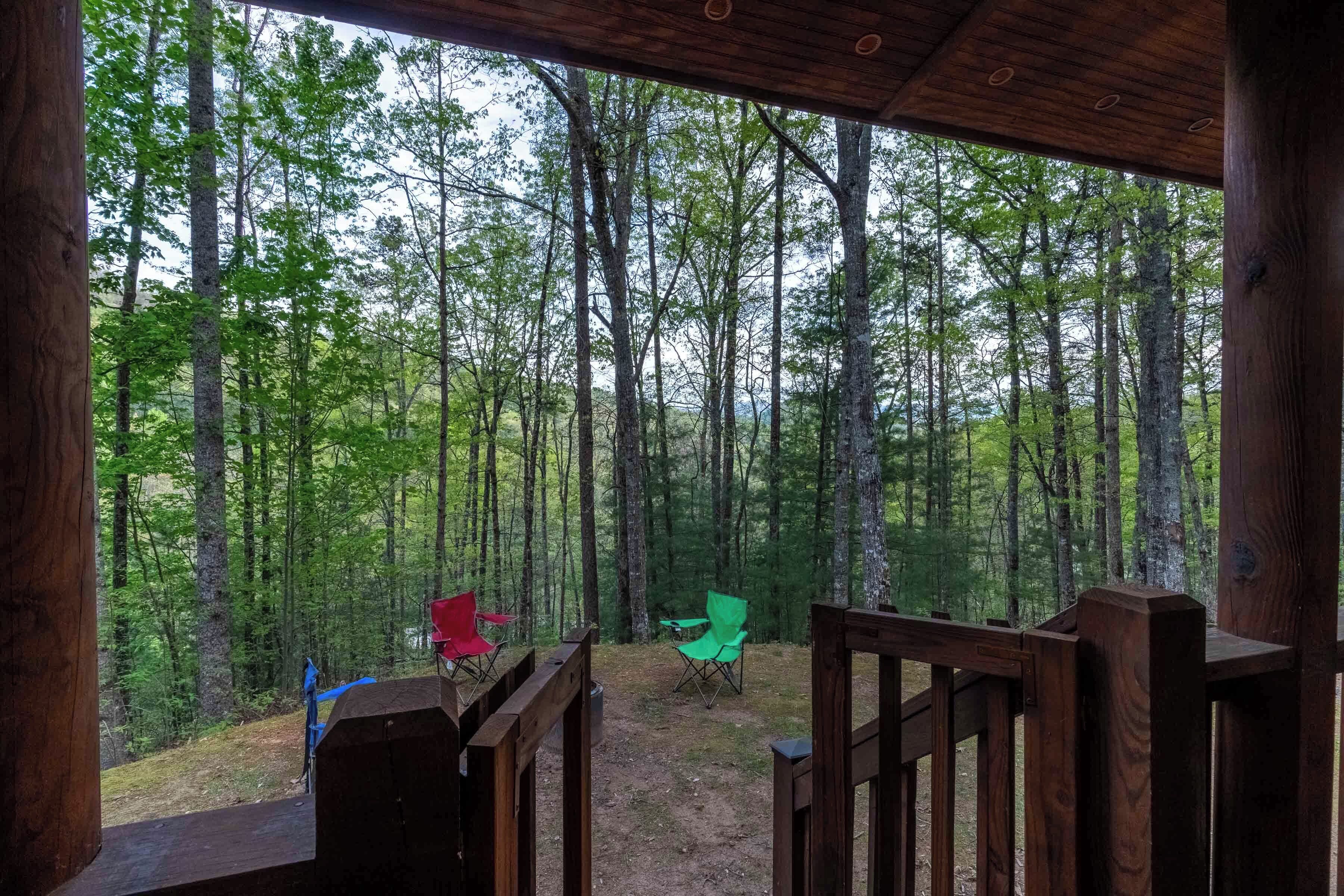 Una terraza de madera con vistas a un bosque. Hay dos sillas plegables verdes y una roja.