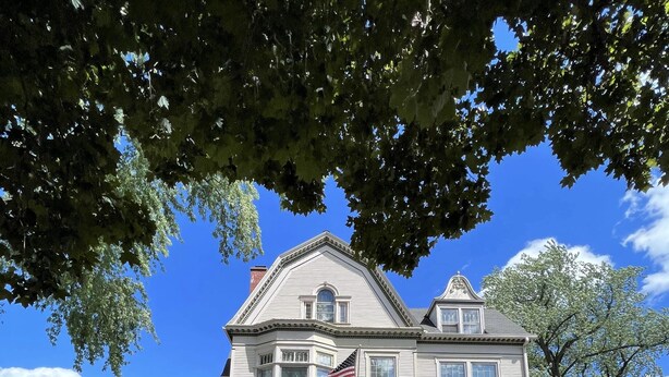 Una casa grande de dos pisos con una bandera estadounidense destacada, fachada de ladrillo y césped cuidado.