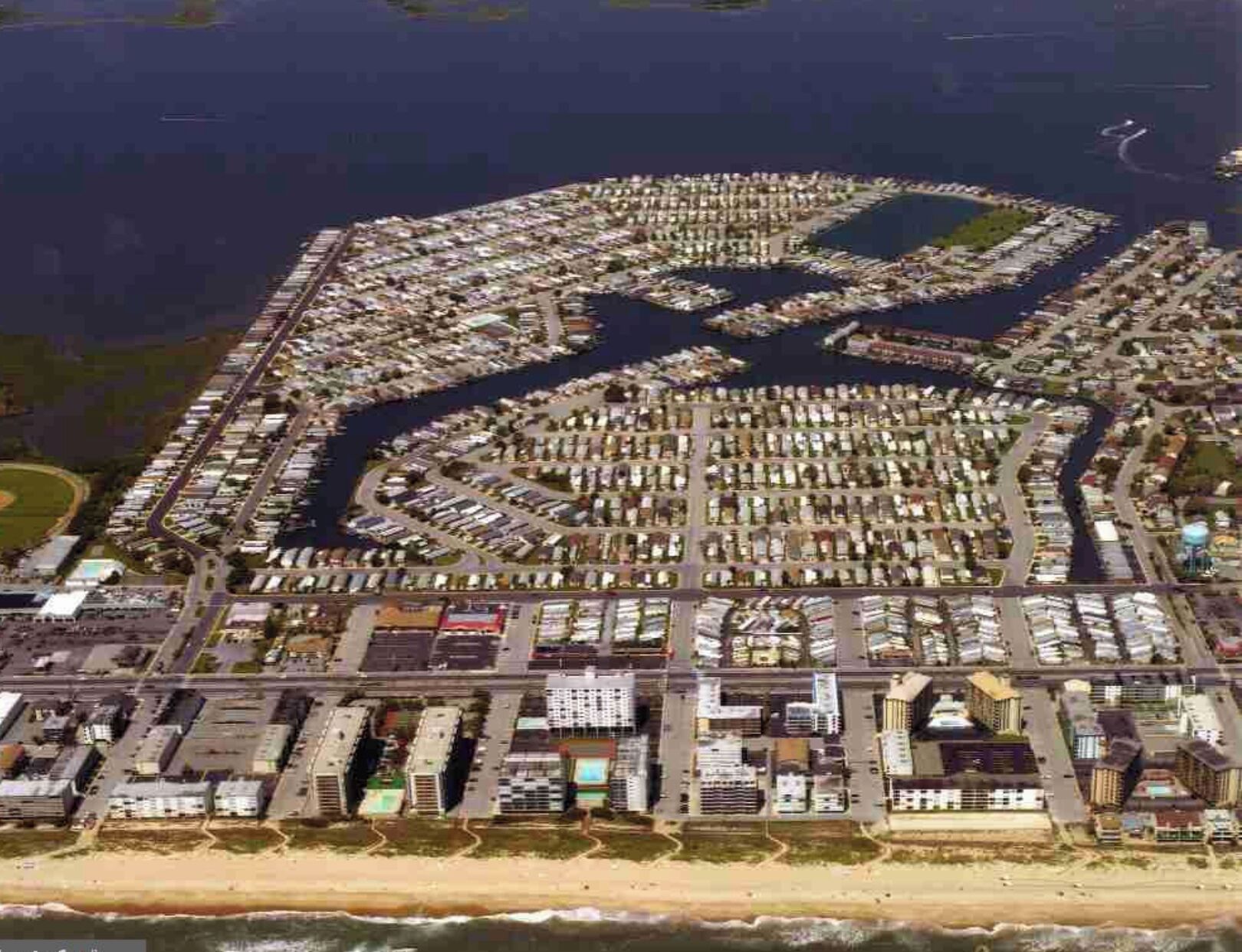 Une vue aérienne d’une grande marina bien aménagée, avec de nombreux quais et des bateaux, entourée d’un quartier résidentiel dense comprenant divers bâtiments.