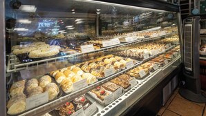 Een bakkerijdisplay met diverse gebakjes en desserts, waaronder kokosroomhoorntjes, amandel amaretti's en pindakaas taartjes.