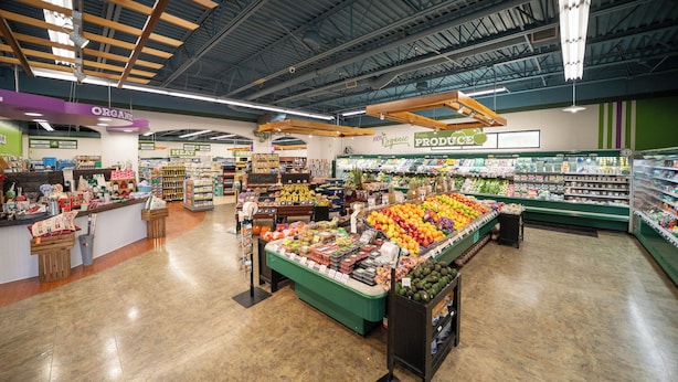 Een supermarktinterieur met een groenteafdeling, een vleesafdeling en verschillende gangpaden.