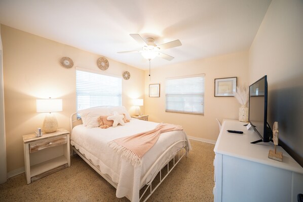 Une chambre à coucher comprenant un lit, des tables de chevet, un bureau, un ventilateur de plafond et des éléments de décoration murale.