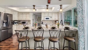 A modern kitchen with white cabinets, stainless steel appliances, and a central island with bar stools. - Resort Backyard w/Private Pool- Spacious Home close to Stadium & Spring Training (Glendale)
