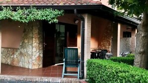 Un edificio de piedra con tejado de baldosas, una silla verde en el exterior y un seto bien cuidado.