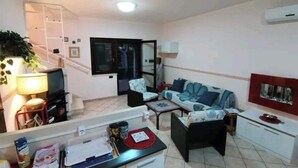 Una sala de estar con sofá, sillas, una mesa de centro, televisor y una escalera que conduce a otra habitación.