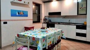 Cocina compacta con gabinetes blancos, salpicadero de azulejos y un comedor con una mesa preparada para dos.