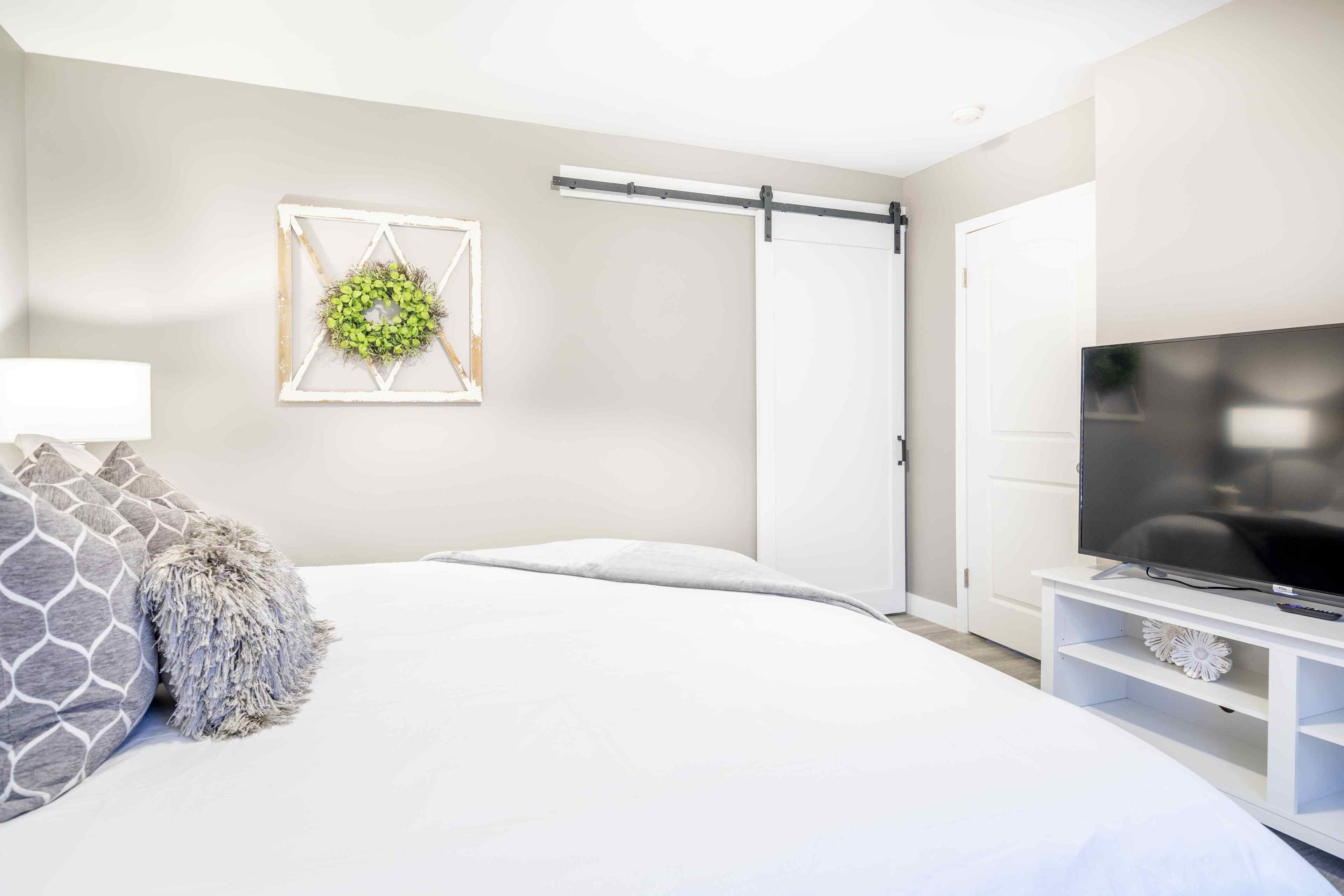 A modern bedroom with a bed, a television on a stand, a sliding door, and a wall decoration.