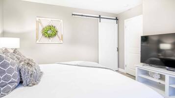 A modern bedroom with a bed, a television on a stand, a sliding door, and a wall decoration.