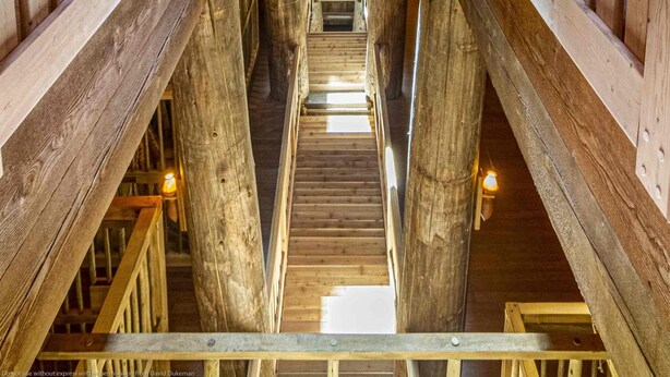 Interior de madera con una escalera central flanqueada por barandillas, que conduce a un nivel superior.
