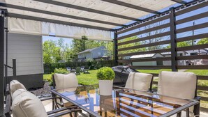 Un patio exterior con una mesa y sillas de vidrio, una parrilla y una zona de estar cubierta.