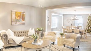 Una sala de estar con un sofá color beige, sillones, una mesa de centro y un comedor con una araña.