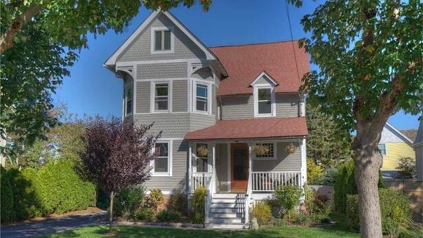 A two-story house with a front porch, a red roof, and a well-maintained lawn.