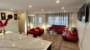 A modern living room with a red sofa, a dining table, and a TV mounted on the wall. - LUXURIOUS 3 BR Home in CENTRAL Calgary b/W AIRPORT & Downtown  (Calgary)