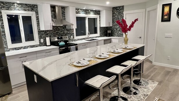 A modern kitchen with a central island, white cabinetry, and a stone backsplash. - LUXURIOUS 3 BR Home in CENTRAL Calgary b/W AIRPORT & Downtown  (Calgary)