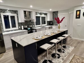 Una cocina moderna con una isla central, armarios blancos y un salpicadero de piedra.