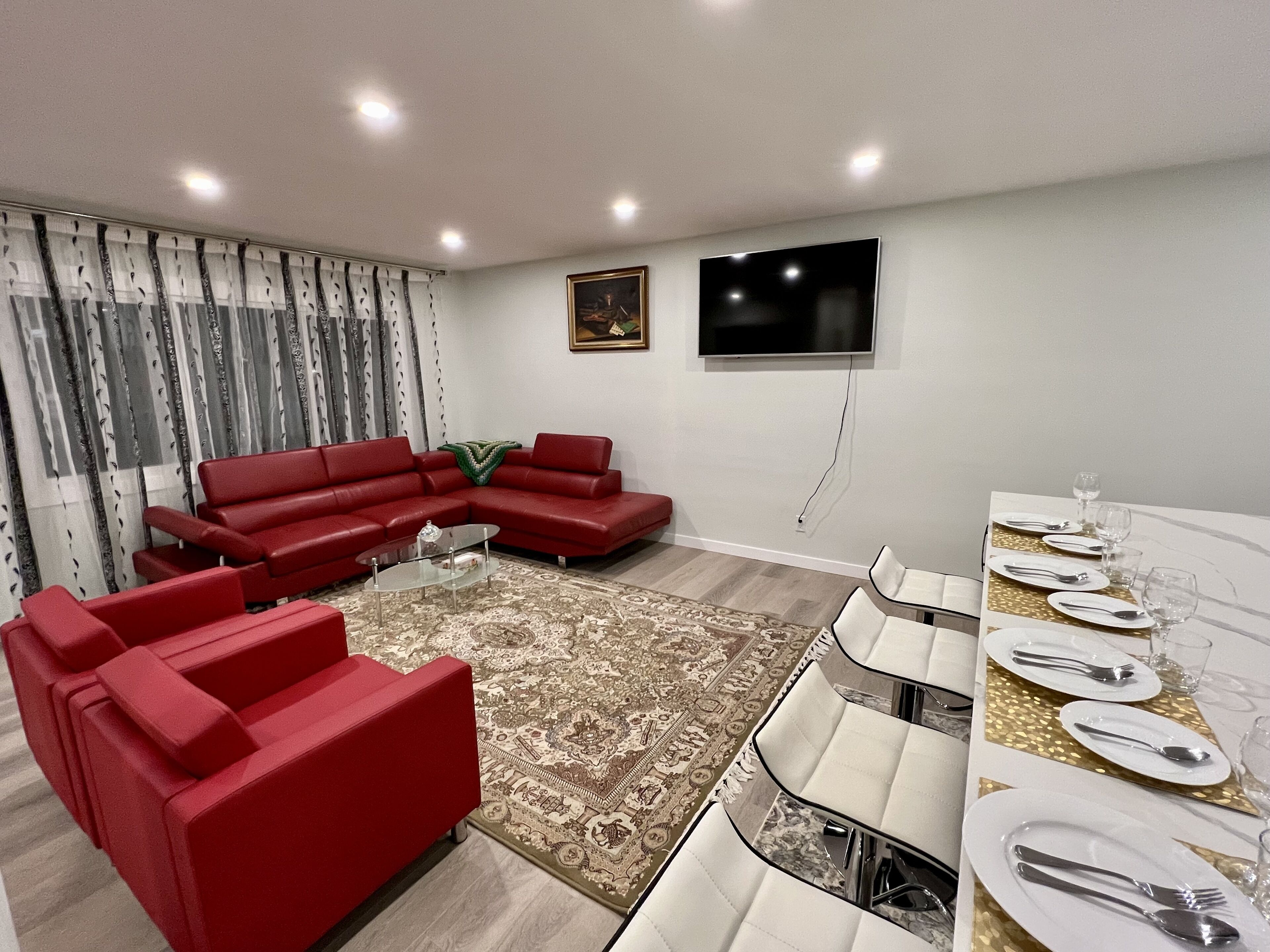 Ein modernes Wohnzimmer mit einem roten Ecksofa, einem Glastisch und einem Essbereich mit weißen Stühlen und einem Tisch für vier Personen.