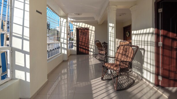 A sunlit corridor with a tiled floor, a wooden door, and two wicker chairs. - Santo Domingo Este Retreat With 2 Bedrooms Apt (Santo Domingo Este)