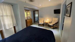 Ein Schlafzimmer mit einem Bett, zwei Stühlen, einem Schreibtisch, einem Deckenventilator und einem Fernseher an der Wand.