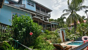 Ein blaues, zweistöckiges Haus mit Balkon, umgeben von üppiger Vegetation und einem Swimmingpool.