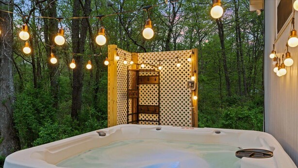 A hot tub surrounded by a wooden structure with lattice walls, set in a forested area.