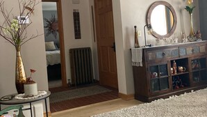 Un salon doté d’un plancher en bois, d’un miroir rond, d’une armoire aux portes vitrées et d’un passage menant à une autre pièce.